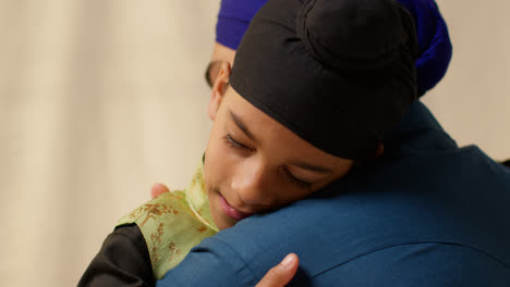 Primer-Plano-De-Estudio-De-Un-Padre-Sikh-Abrazando-A-Su-Hijo,-Ambos-Con-Turbante,-Contra-Un-Fondo-Liso-1